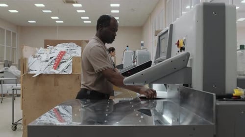 Senior Black Man Using Paper Cutter At Work