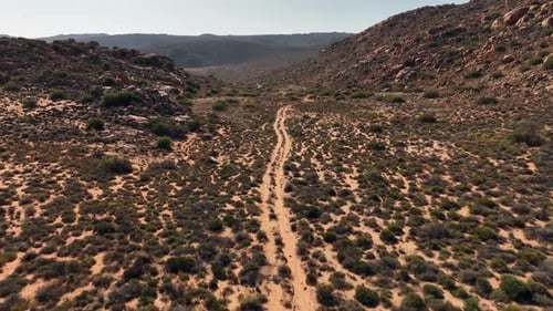 Rough 4x4 road traverses hilly red sand desert landscape, aerial view