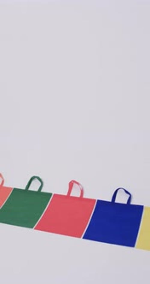 Vídeo vertical de una fila de bolsas de lona multicolores con espacio para copiar sobre fondo blanco