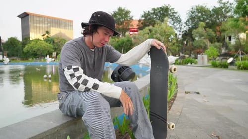 Young Man Relaxing with Skateboard in Urban Park