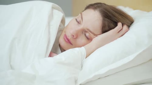 Close up portrait of sleeping woman in bed at home wakes up from the loud sound of the alarm clock
