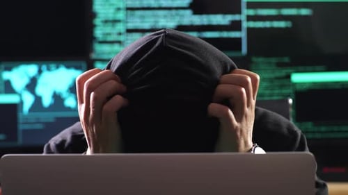 Primer plano de un hacker asiático con capucha que tiene dolor de cabeza mientras trabaja en una computadora portátil con mapas y datos