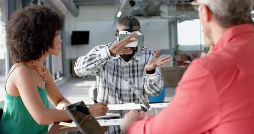African american businessman wearing vr headset, gesturing while colleagues watching him at office