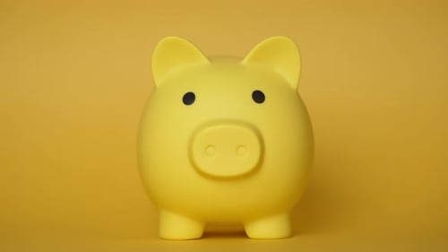 Hand inserting coins into yellow piggy bank on yellow background