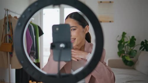 Mujer bloguera filmando un tutorial de maquillaje usando un teléfono celular en su casa de cerca. Chica influencer parlante G...