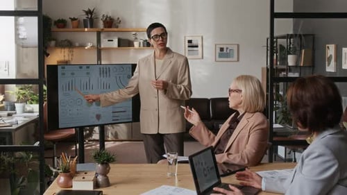 Middle-Aged Woman Giving Presentation During Meeting with Colleagues in Office