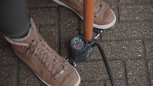 Frau, die auf einer Fahrradluftpumpe steht, unterstützt, während sie den Luftdruck in ihren Fahrradreifen hochpumpt.