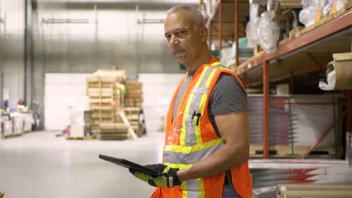 Smiling african american supervisor holding tablet standing proudly in warehouse