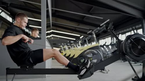 Athletic Man Focused While Training on Rowing Machine in Gym