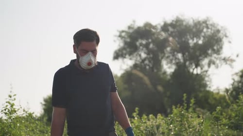 Gärtner mit Maske steht zwischen Pflanzen und ist bereit, den Garten zu begasen