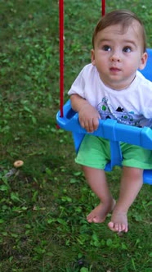 Small kid looking up while swaying on the swing.