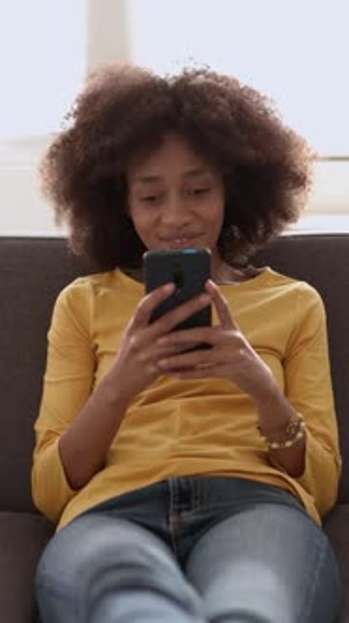 Smiling Woman Using Smartphone on Sofa Indoors