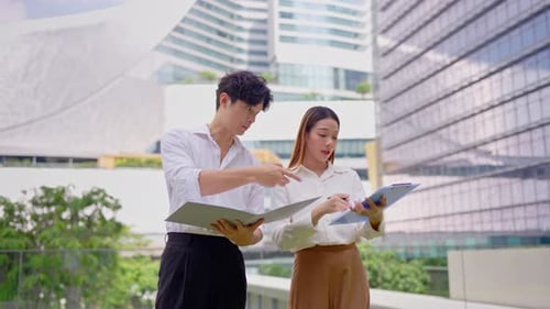 Asian young businessman and woman partner working outdoors in the city.