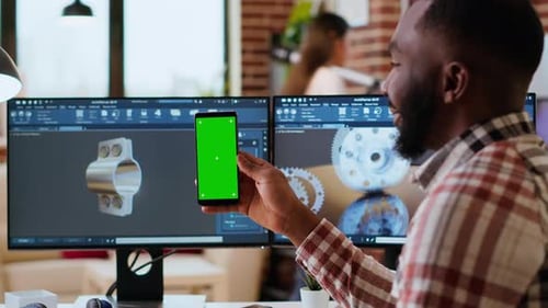 Software Developer Creates a Gear Prototype on Dual Monitors Next to Chroma Key