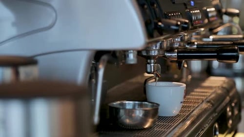 A close-up of an espresso pouring coffee into a white cup in a cozy café setting