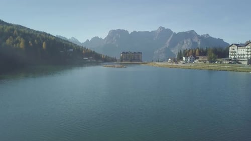 Aerial drone shot flying fast over the blue water of an alpine lake in a resort village in Italy wit