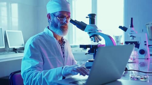 Scientist Uses Microscope and Laptop in Laboratory