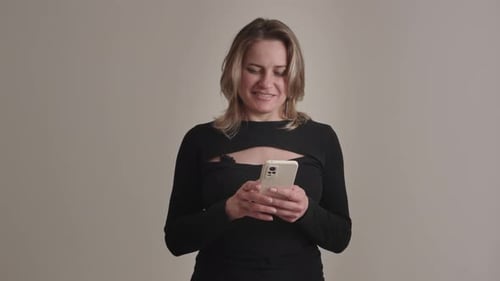 A Stylish Woman in Black Attire Using Smartphone in Modern Studio Merging Technology and Fashion