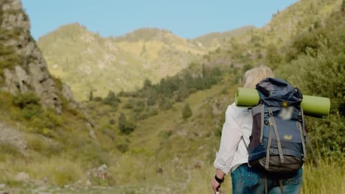 Senior Woman with a Backpack and Hiking Sticks Slowly Walks Along a Trail Surrounded By Majestic