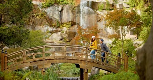 Couple Walking Over Wooden Bridge Near Waterfall