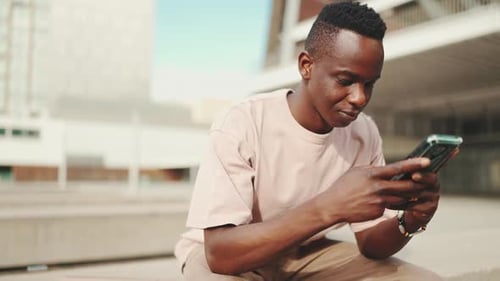Young student sits outside of university, uses cellphone, taps on smartphone screen