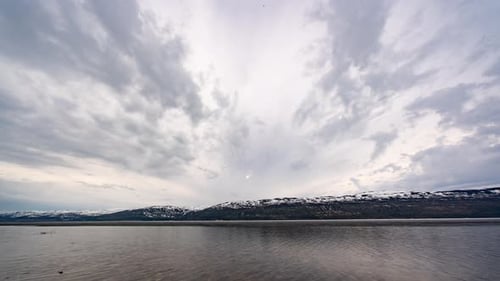 Clouds flying above the icy lake. Snow-covered mountains on the background.