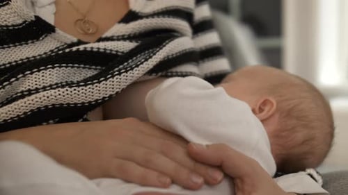Close view of baby breastfeeding while held in the arms of mother