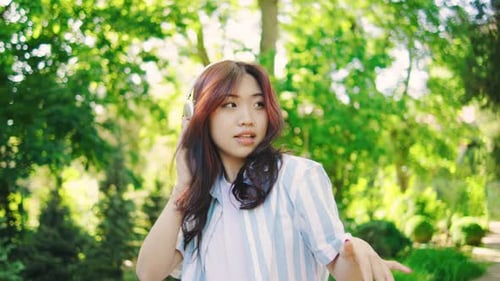 Joyful Young Asian Woman Dancing Energetically to Music on Headphones in Green Park