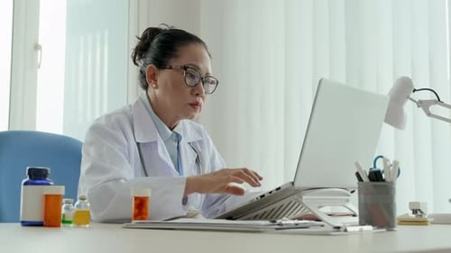 Mature Doctor Giving Online Consultations to Patients in Medical Office