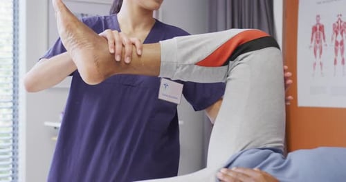 Diverse female physiotherapist and senior male patient in hospital physical therapy session on leg