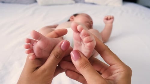 Baby's Feet Being Massaged on White Bed