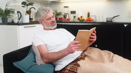 Man Relaxing on Sofa Reading Book Indoors