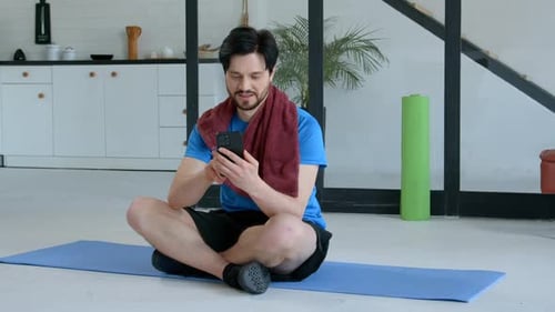 Man on Exercise Mat Uses Phone in Home