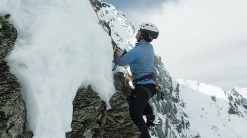 Ice climber clambering over exposed rocky area, roped climbing in Alps