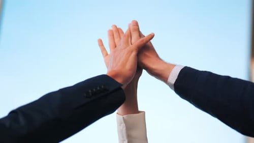 Low angle shot of 3 Businesspeople Clap Hands in a Triangle Under Blue Sky