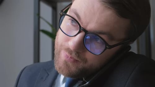 Man in Suit with Tie and Glasses Talking on Cell in Office