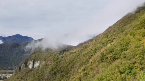 Aerial shot of cloudscape and fog covering green mountain rocks in nature. Beautiful sunny day with