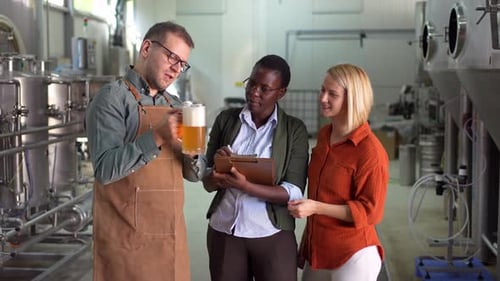 Brewmaster presenting a glass of beer to two female quality control inspectors at a brewery
