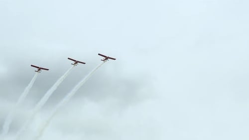 Three red aerobatic aircrafts carrying out dynamic maneuvers in front of spectators at Baltic