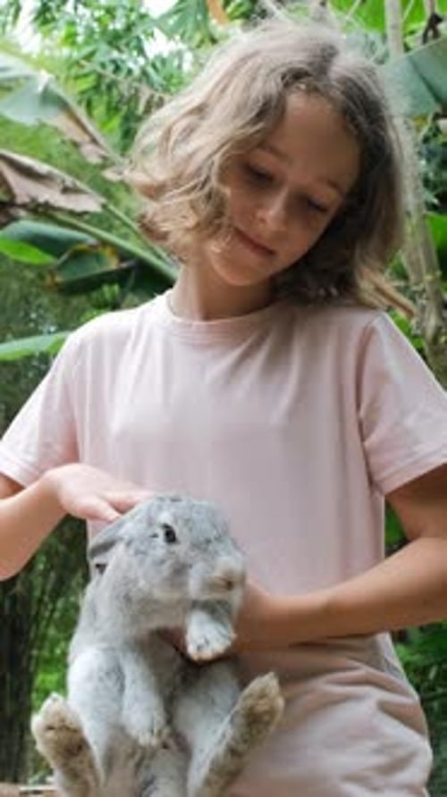 Jovem garota acariciando coelho em terras agrícolas tropicais
