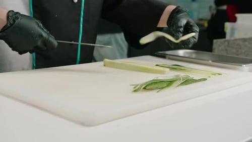 Close-up of a sushi maker in gloves cutting a cucumber with a professional kitchen knife on a board
