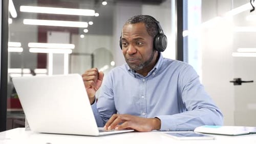 Man Celebrates Success at Laptop in Modern Office