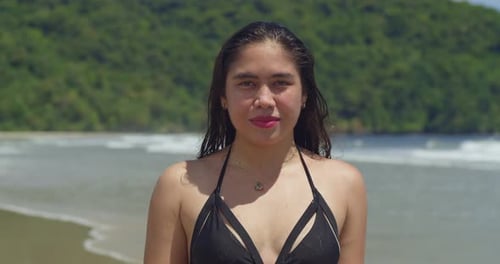 Un entorno de playa tropical presenta a una mujer joven con confianza, vestida con un elegante bikini tipo tanga