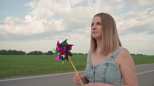 Thoughtful Woman Walking with Pinwheel on Rural Road