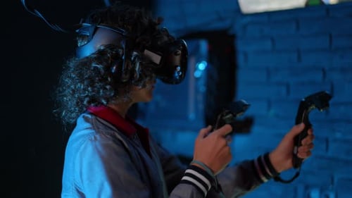 Dans une pièce faiblement éclairée d'un club de réalité virtuelle, un adolescent avec des lunettes de réalité virtuelle et des manettes à la main joue