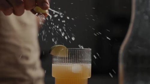 Junges Männchen, das Limette oder Zitrone über einen frisch gemischten Cocktail in einem Trinkglas auspresst 4K Zeitlupe Schließen