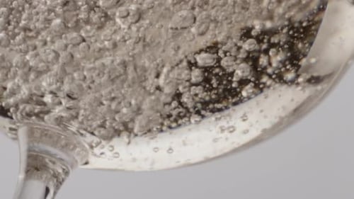 Sparkling Wine Fizzing on Clear Glass Bottom Close Up. Golden Champagne Bubbling