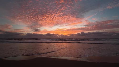 Dramatisch Sonnenaufgang über den Meereswellen mit feurigen Wolken und feuchten Sandreflexionen.