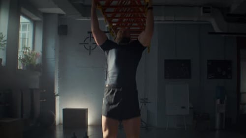 Starker Mann in schwarzer Sportkleidung macht Klimmzüge am Metallträger im Fitnessstudio