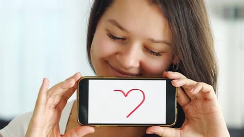 Woman Draws Heart on Phone Screen with Smile